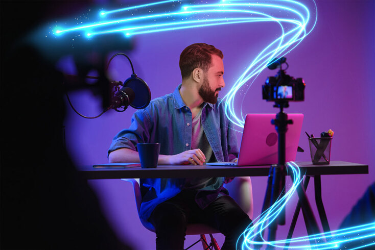 Άνδρας καθισμένος σε γραφείο με ανοιχτό laptop και φωτογραφική μηχανή μπροστά του