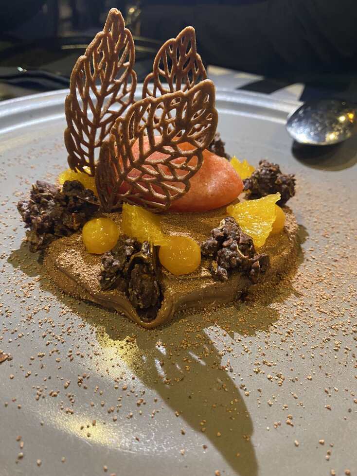 Κρεμέ σοκολάτας γάλακτος με κραμπλ δημητριακών, τζελ μάνγκο, φιλέτο πορτοκάλι, τουίλ κακάο και σορμπέ σαγκουίνι 