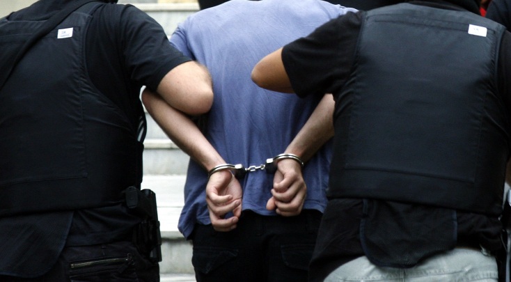 Αστυνομικοί κρατούν άτομο που φέρει χειροπέδες 
