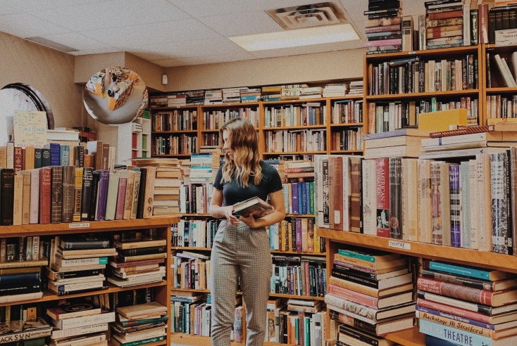 Νεαρή γυναίκα σε βιβλιοπωλείο εξετάζει προσεκτικά τα βιβλία που επιθυμεί να αγοράσει