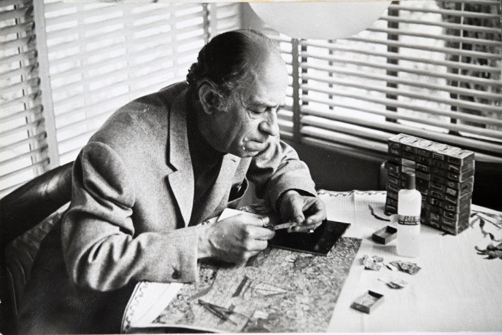 Ο Μίμης Φωτόπουλος σε τραπέζι όπου έχει τα σύνεργά του για την Τέχνη του κολάζ στην οποία αφιερώθηκε παράλληλα με την υποκριτική