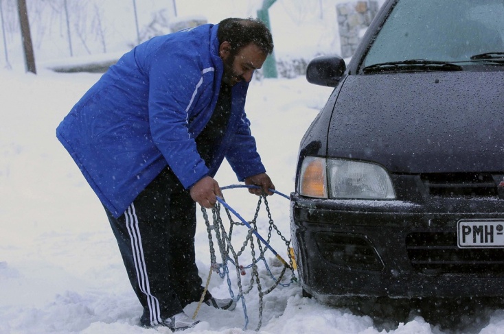Άνδρας τοποθετεί αντιολισθητικές αλυσίδες στο όχημά του