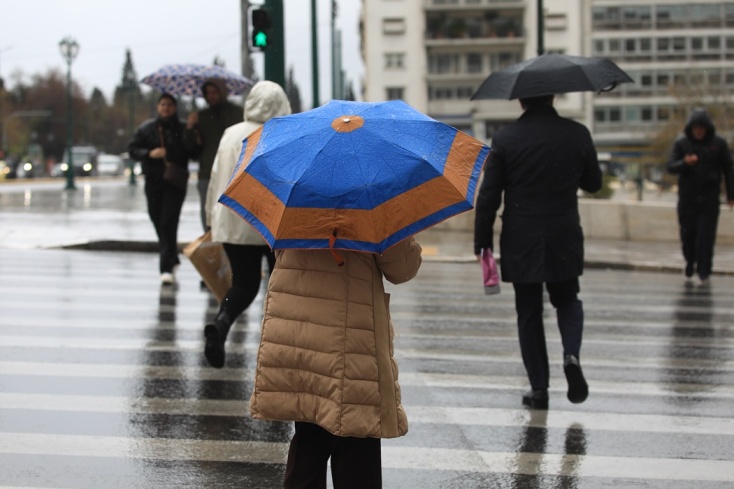 Άτομα με ομπρέλα περπατούν στο κέντρο της Αθήνας