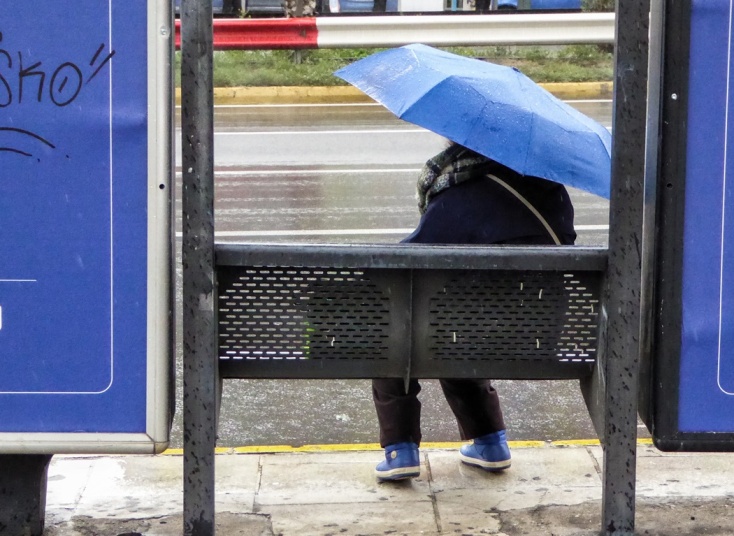 Γυναίκα με ομπρέλα σε στάση λεωφορείου ενώ βρέχει