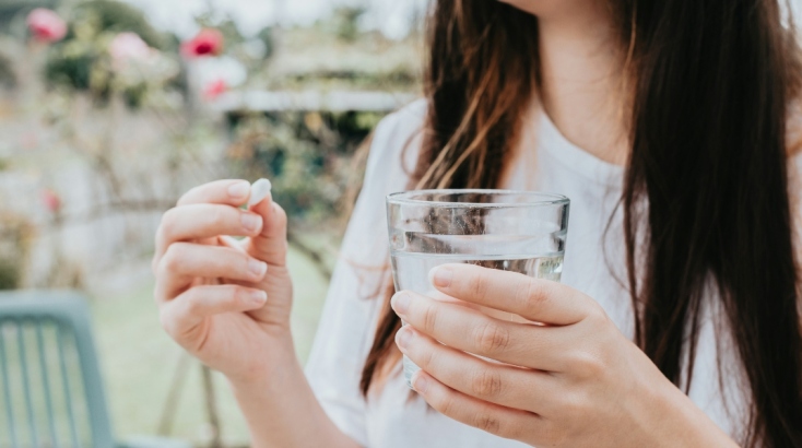 Γυναίκα κρατά χάπι για την ημικρανία και ένα ποτήρι νερό 