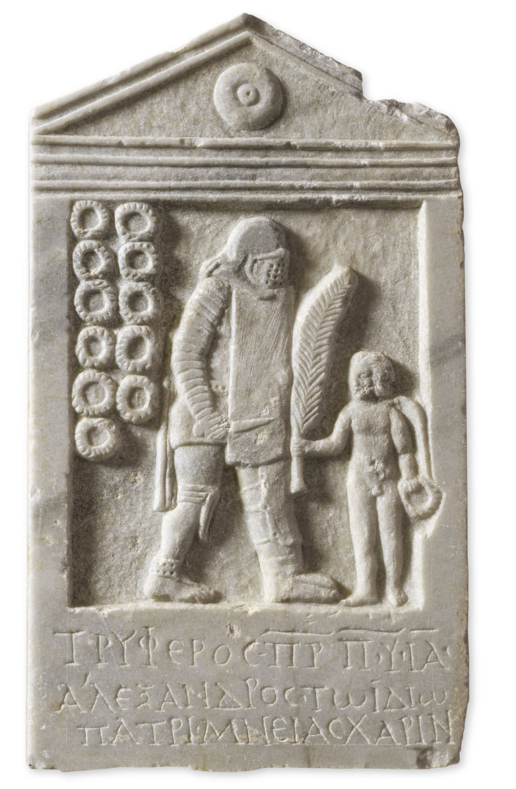 Μαρμάρινη επιτύμβια στήλη του μονομάχου Τρύφερου, την οποία προσέφερε στη μνήμη του ο γιος του Αλέξανδρος. Ο μονομάχος, βαριά οπλισμένος, στον τύπο του διώκτη, στρέφεται προς τα δεξιά. Αριστερά της παράστασης, έντεκα στεφάνια συμβολίζουν τις νίκες του στον στίβο. Πάτρα, βόρειο νεκροταφείο, 2ος-3ος αι. μ.Χ.
