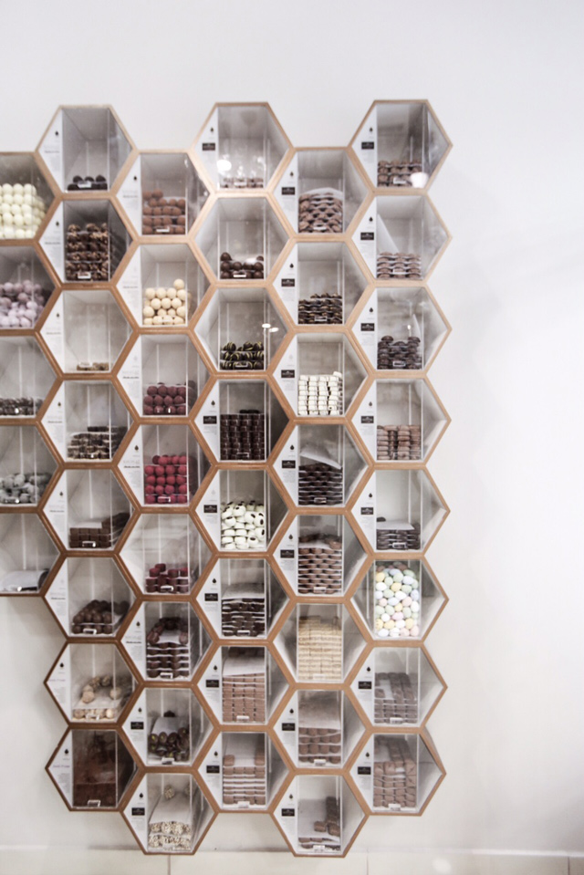 Τα ράφια-κυψέλες γεμάτα με δεκάδες σοκολατάκια της Valhrona και του Xocolat Manufactur Τα ράφια-κυψέλες γεμάτα με δεκάδες σοκολατάκια της Valhrona και του Xocolat Manufactur