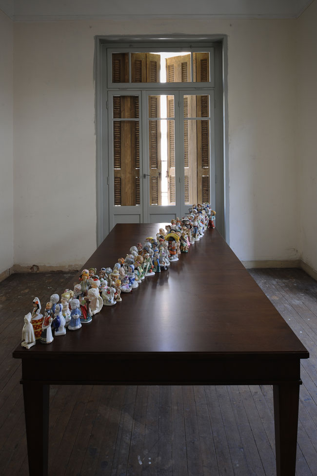 Αικατερίνη Γεγησιάν Το προσφυγάκι (2017), διαστάσεις μεταβλητές 120 ευρεθέντα αγαλματίδια, πορσελάνη, πηλός, γύψος, ρητίνη, ξύλινο τραπέζι