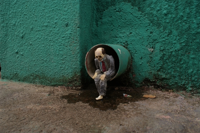 O Isaac Cordal, γεννημένος το 1974, είναι Ισπανός καλλιτέχνης από τη Γαλικία και ζει στις Βρυξέλλες. Τα έργα του συνδυάζουν τη μικρογλυπτική με τη φωτογραφία μέσα στο αστικό τοπίο. Έχει σπουδάσει γλυπτική, έχει ειδικευτεί στην τεχνική της πέτρας και υπήρξε μέλος καλλιτεχνικών ομάδων, γκρουπ της death metal μουσικής σκηνής της Ισπανίας καθώς και εκδότης του fanzine Exorcism. Αυτό που κάνει ο Ισπανός καλλιτέχνης είναι κάτι περισσότερο από urban art. Θα έλεγε κανείς ότι είναι ένα παιχνίδι «κρυμμένου θησαυρού», η δημιουργία ενός μικρόκοσμου μέσα στην πόλη και στις μυστικές γωνιές της. Δημιουργεί μικρές ανθρώπινες φιγούρες (περίπου 15 εκ. ύψος) από πηλό, κατασκευάζει καλούπια και μετά τις μετατρέπει σε φιγούρες από τσιμέντο, συνήθως ανθρώπους businessmen με καφκική διάθεση, που τους στήνει σε πόζες, μόνους ή όλους μαζί στο σύμπαν της πόλης, σατιρίζοντας σκληρά τον σύγχρονο κόσμο, την κλιματική αλλαγή, τη γραφειοκρατία, τη μοναξιά. Συνήθως είναι δύσκολο να τα ανακαλύψεις με την πρώτη ματιά, πρέπει να ψάξεις ιδιαίτ O Isaac Cordal, γεννημένος το 1974, είναι Ισπανός καλλιτέχνης από τη Γαλικία και ζει στις Βρυξέλλες. Τα έργα του συνδυάζουν τη μικρογλυπτική με τη φωτογραφία μέσα στο αστικό τοπίο. Έχει σπουδάσει γλυπτική, έχει ειδικευτεί στην τεχνική της πέτρας και υπήρξε μέλος καλλιτεχνικών ομάδων, γκρουπ της death metal μουσικής σκηνής της Ισπανίας καθώς και εκδότης του fanzine Exorcism. Αυτό που κάνει ο Ισπανός καλλιτέχνης είναι κάτι περισσότερο από urban art. Θα έλεγε κανείς ότι είναι ένα παιχνίδι «κρυμμένου θησαυρού»
