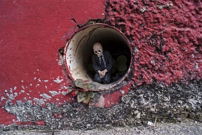 O Isaac Cordal, γεννημένος το 1974, είναι Ισπανός καλλιτέχνης από τη Γαλικία και ζει στις Βρυξέλλες. Τα έργα του συνδυάζουν τη μικρογλυπτική με τη φωτογραφία μέσα στο αστικό τοπίο. Έχει σπουδάσει γλυπτική, έχει ειδικευτεί στην τεχνική της πέτρας και υπήρξε μέλος καλλιτεχνικών ομάδων, γκρουπ της death metal μουσικής σκηνής της Ισπανίας καθώς και εκδότης του fanzine Exorcism. Αυτό που κάνει ο Ισπανός καλλιτέχνης είναι κάτι περισσότερο από urban art. Θα έλεγε κανείς ότι είναι ένα παιχνίδι «κρυμμένου θησαυρού», η δημιουργία ενός μικρόκοσμου μέσα στην πόλη και στις μυστικές γωνιές της. Δημιουργεί μικρές ανθρώπινες φιγούρες (περίπου 15 εκ. ύψος) από πηλό, κατασκευάζει καλούπια και μετά τις μετατρέπει σε φιγούρες από τσιμέντο, συνήθως ανθρώπους businessmen με καφκική διάθεση, που τους στήνει σε πόζες, μόνους ή όλους μαζί στο σύμπαν της πόλης, σατιρίζοντας σκληρά τον σύγχρονο κόσμο, την κλιματική αλλαγή, τη γραφειοκρατία, τη μοναξιά. Συνήθως είναι δύσκολο να τα ανακαλύψεις με την πρώτη ματιά, πρέπει να ψάξεις ιδιαίτ O Isaac Cordal, γεννημένος το 1974, είναι Ισπανός καλλιτέχνης από τη Γαλικία και ζει στις Βρυξέλλες. Τα έργα του συνδυάζουν τη μικρογλυπτική με τη φωτογραφία μέσα στο αστικό τοπίο. Έχει σπουδάσει γλυπτική, έχει ειδικευτεί στην τεχνική της πέτρας και υπήρξε μέλος καλλιτεχνικών ομάδων, γκρουπ της death metal μουσικής σκηνής της Ισπανίας καθώς και εκδότης του fanzine Exorcism. Αυτό που κάνει ο Ισπανός καλλιτέχνης είναι κάτι περισσότερο από urban art. Θα έλεγε κανείς ότι είναι ένα παιχνίδι «κρυμμένου θησαυρού»