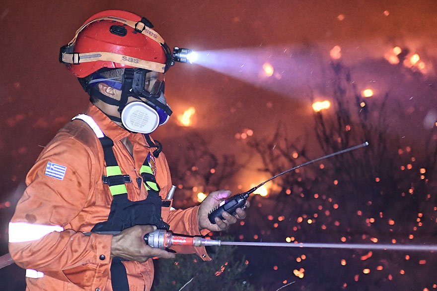 Πυροσβέστης με μάσκα στο πρόσωπο και τον ασύρματο στο χέρι επιχειρεί στη φωτιά στην Κορινθία