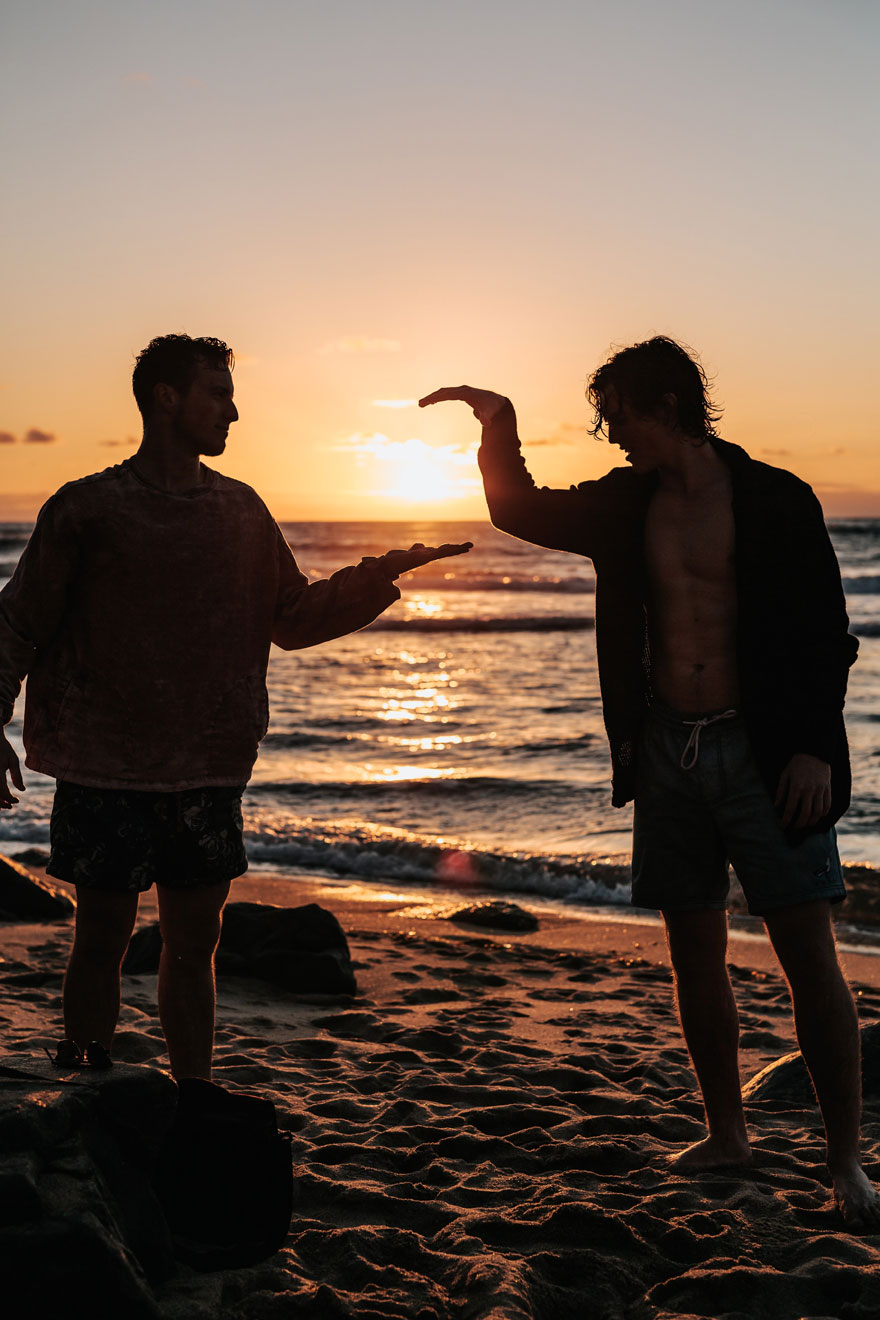 Δύο σκοτεινές φιγούρες αντρών με φόντο το ηλιοβασίλεμα και τη θάλασσα δίνουν τα χέρια τους